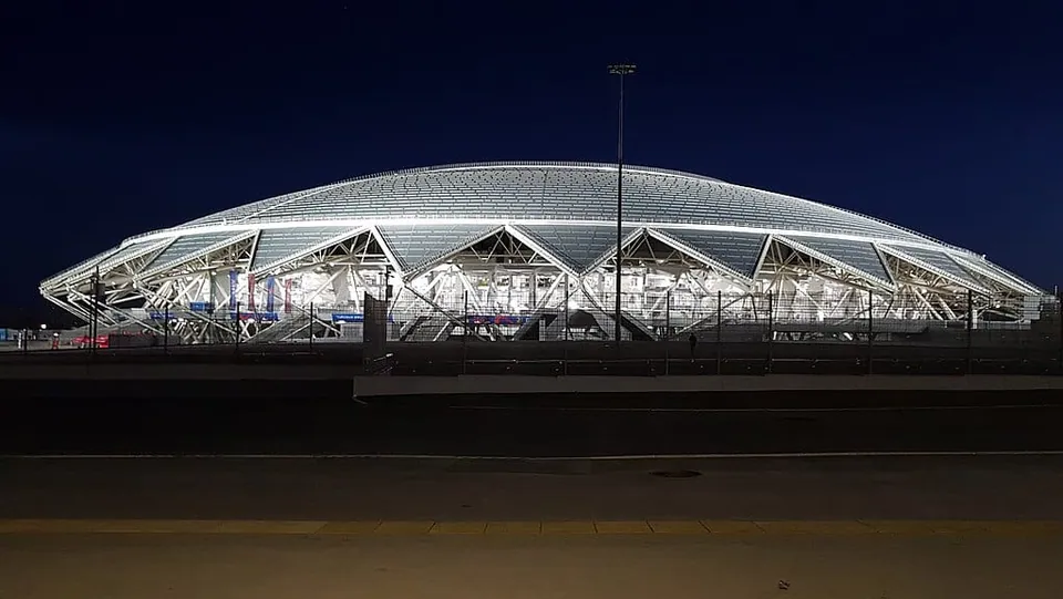 สนามกีฬา Cosmos Arena ที่มีหลังคาโค้งทรงโดมและโครงสร้างโครงเหล็กสามเหลี่ยมเรียงรายตามตัวอาคาร ซึ่งถูกส่องสว่างด้วยไฟสีขาวตัดกับท้องฟ้ามืดในเวลากลางคืน