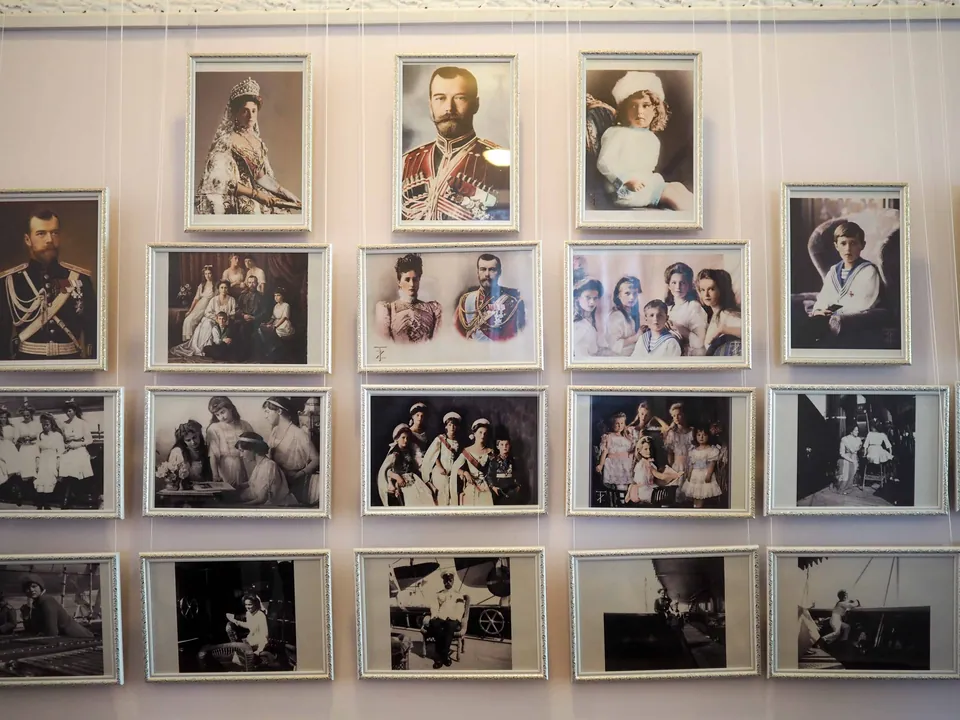 ภาพถ่ายขาวดำและสีในกรอบรูปหลายใบแขวนเรียงกันบนผนัง แสดงภาพบุคคลในชุดเครื่องแบบทหารและชุดราตรี