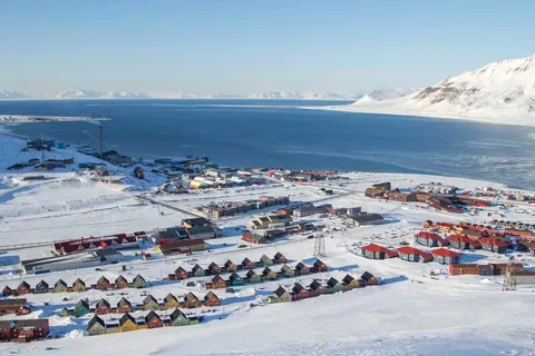 ภาพมุมสูงของเมืองลองเยียร์เบียน (Longyearbyen) ที่ปกคลุมด้วยหิมะ มีบ้านหลังเล็กหลังใหญ่เรียงรายอยู่ริมชายฝั่งน้ำสีฟ้า