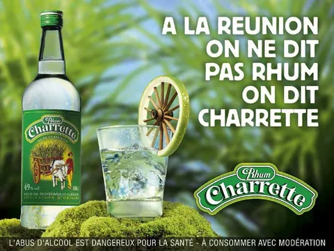 ขวดเหล้า Rhum Charrette วางข้างแก้วน้ำแข็งที่มีมะนาวฝานเป็นรูปล้อเกวียน พร้อมข้อความภาษาฝรั่งเศสบนพื้นหลังใบไม้เขียว