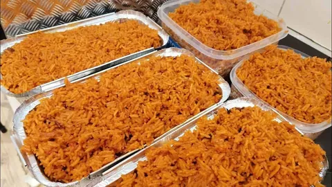 ข้าวหมกสีส้มจัดบรรจุในถาดอะลูมิเนียมและกล่องพลาสติกใสหลายใบ วางเรียงกันบนพื้นผิวโลหะ