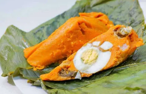 อาหารสีส้มวางบนใบไม้สีเขียว มีไข่ต้มสีขาวและไข่แดงสีเหลืองตัดครึ่งวางอยู่ด้านบน