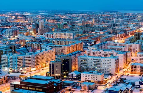 ภาพมุมสูงของเมือง Yakutsk ในประเทศรัสเซียตอนกลางคืน มีอาคารสูงหลายหลังเรียงรายกันและถนนที่สว่างไสวด้วยไฟสีส้ม