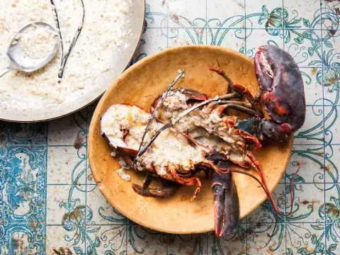 กุ้งล็อบสเตอร์ที่ผ่าเปิดและราดซอสสีขาววางอยู่ในชามสีเหลืองอ่อนบนพื้นกระเบื้องลายดอกไม้