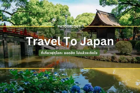 สะพานสีแดงทอดข้ามแม่น้ำที่มีต้นฮอกกิดะสีน้ำเงินอยู่ริมตลิ่ง ด้านหลังมีอาคารหลังคาแบบญี่ปุ่นและต้นไม้เขียวขจี