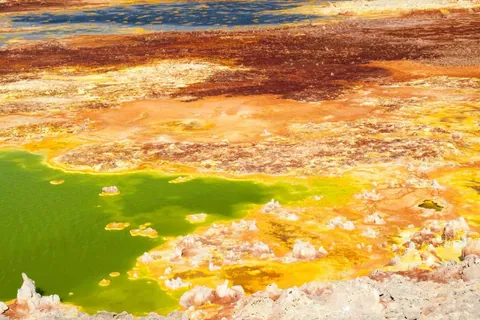 ภาพพื้นดินที่มีสีส้มและเหลืองสลับกับแอ่งน้ำสีเขียวสดใส มีก้อนหินสีขาวกระจายอยู่ตามขอบ