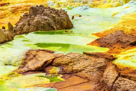 ภาพแอ่งน้ำสีเขียวอมเหลืองไหลผ่านพื้นที่หินสีน้ำตาลและสีส้มที่มีพื้นผิวขรุขระ