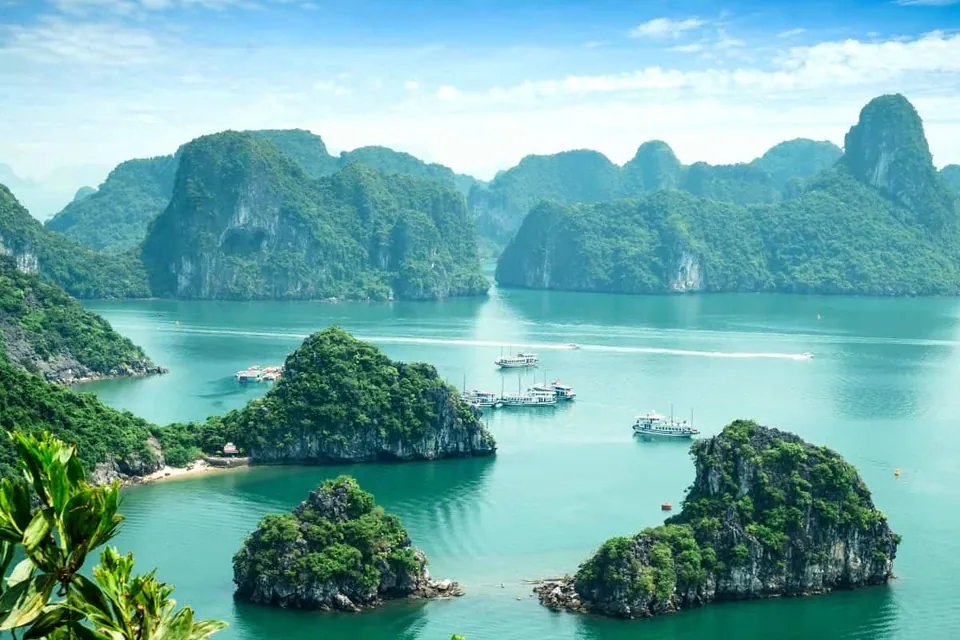ทิวทัศน์ทะเลสีเขียวมรกตที่มีเกาะหินปูนปกคลุมด้วยพืชสีเขียวตั้งอยู่กลางน้ำ และมีเรือหลายลำลอยอยู่