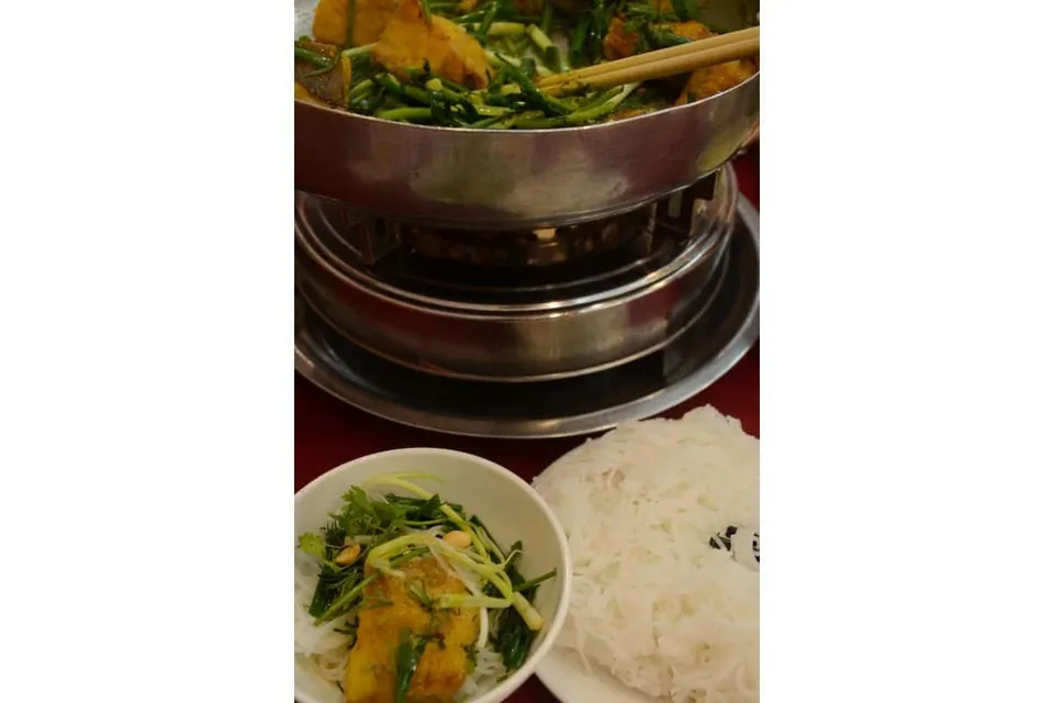 หม้อโลหะบนเตาพร้อมผักและไม้จิ้มฟัน วางข้างชามผักและจานเส้นสีขาว