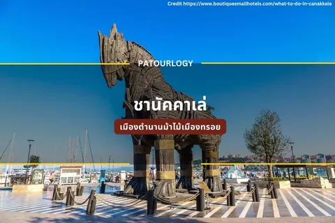 รูปปั้นม้าไม้ขนาดใหญ่ตั้งอยู่บนพื้นกระเบื้องลายทางสีขาวดำ โดยมีเรือใบและอาคารเมืองอยู่เบื้องหลัง