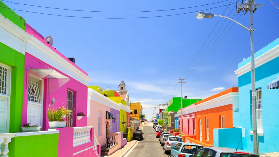 ถนนที่มีบ้านสีชมพู เขียว ส้ม และฟ้าตั้งเรียงกันสองฝั่ง