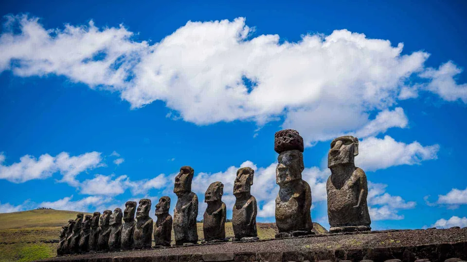 รูปปั้นหินรูปคนหลายองค์เรียงกันเป็นแถวบนฐานหินสีเข้ม ภายใต้ท้องฟ้าสีน้ำเงินที่มีเมฆสีขาวลอยอยู่