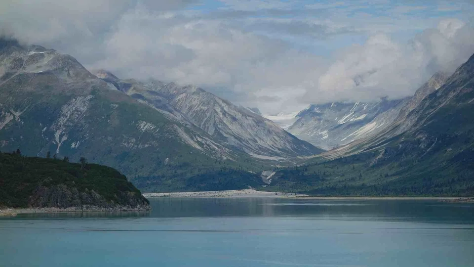 ภาพทิวทัศน์ของทะเลสาบสีฟ้าที่ทอดตัวอยู่ระหว่างเทือกเขาสูงชันปกคลุมด้วยป่าไม้และหิมะ โดยมีเมฆลอยปกคลุมท้องฟ้า
