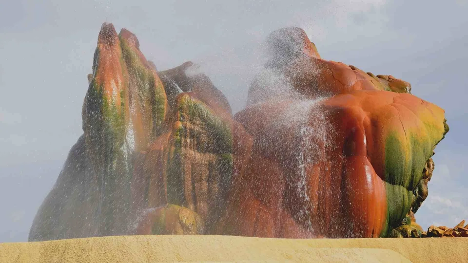 ภาพหินรูปทรงสูงที่มีสีแดงและเขียว มีละอองน้ำสีขาวพ่นออกมาจากด้านบนของหิน