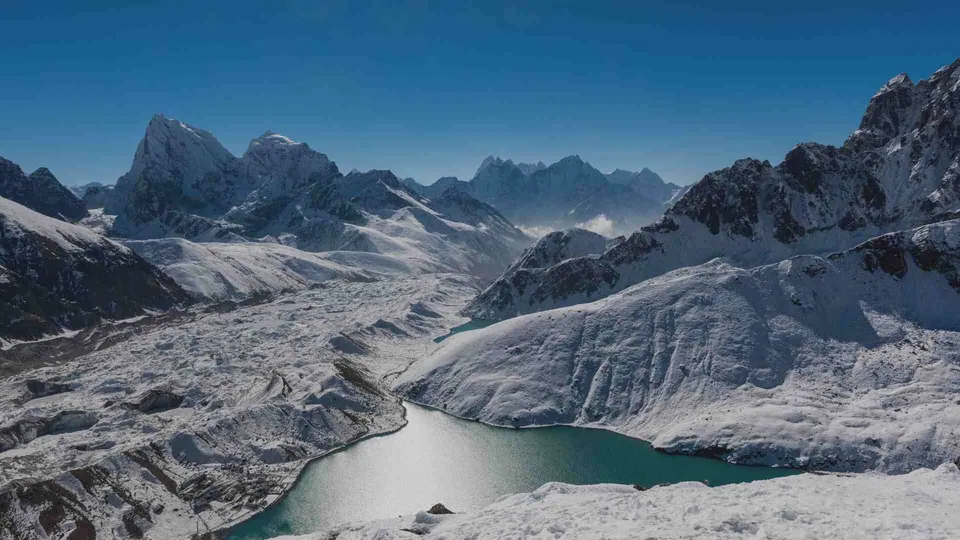 ทัศนียภาพภูเขาหิมะที่มียอดแหลมสูงโอบล้อมทะเลสาบน้ำสีฟ้าอมเขียวในหุบเขา ใต้ท้องฟ้าสีน้ำเงินเข้ม