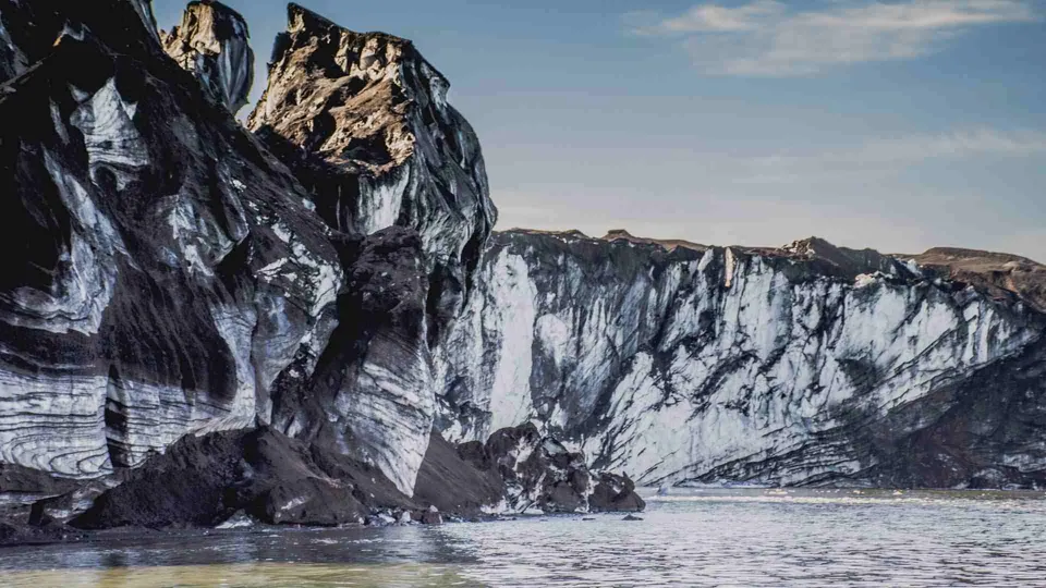 Deception Island: ภูเขาหินสีดำและสีขาวตั้งตระหง่านริมทะเล ใต้ท้องฟ้าสีฟ้าอ่อน