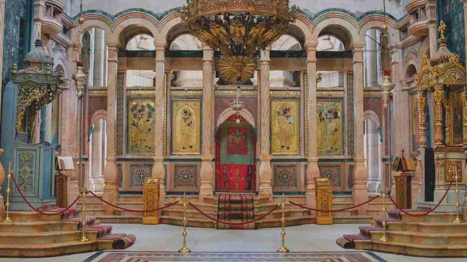 ภาพภายในอาคารที่มีผนังสีชมพูและเสาหินอ่อน มีภาพวาดสีทองติดผนังหลายภาพ ประตูสีแดงอยู่ตรงกลาง และโคมไฟทองห้อยจากเพดาน