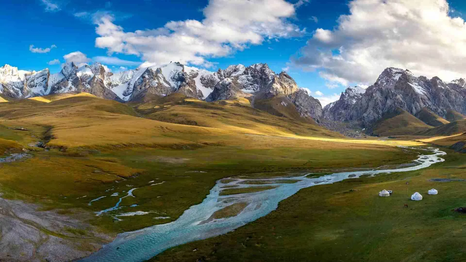 ภาพทิวทัศน์ภูเขาหิมะสูงตระหง่านทอดยาวเป็นแนว มีทุ่งหญ้าสีเขียวและสีเหลืองทอดตัวอยู่เบื้องล่าง โดยมีลำธารน้ำสีฟ้าไหลคดเคี้ยวผ่านกลางทุ่ง